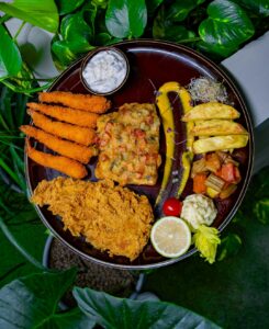 A mixed seafood platter with golden shrimp, fried fish, hush puppies, coleslaw, lemon wedges, and dipping sauce.