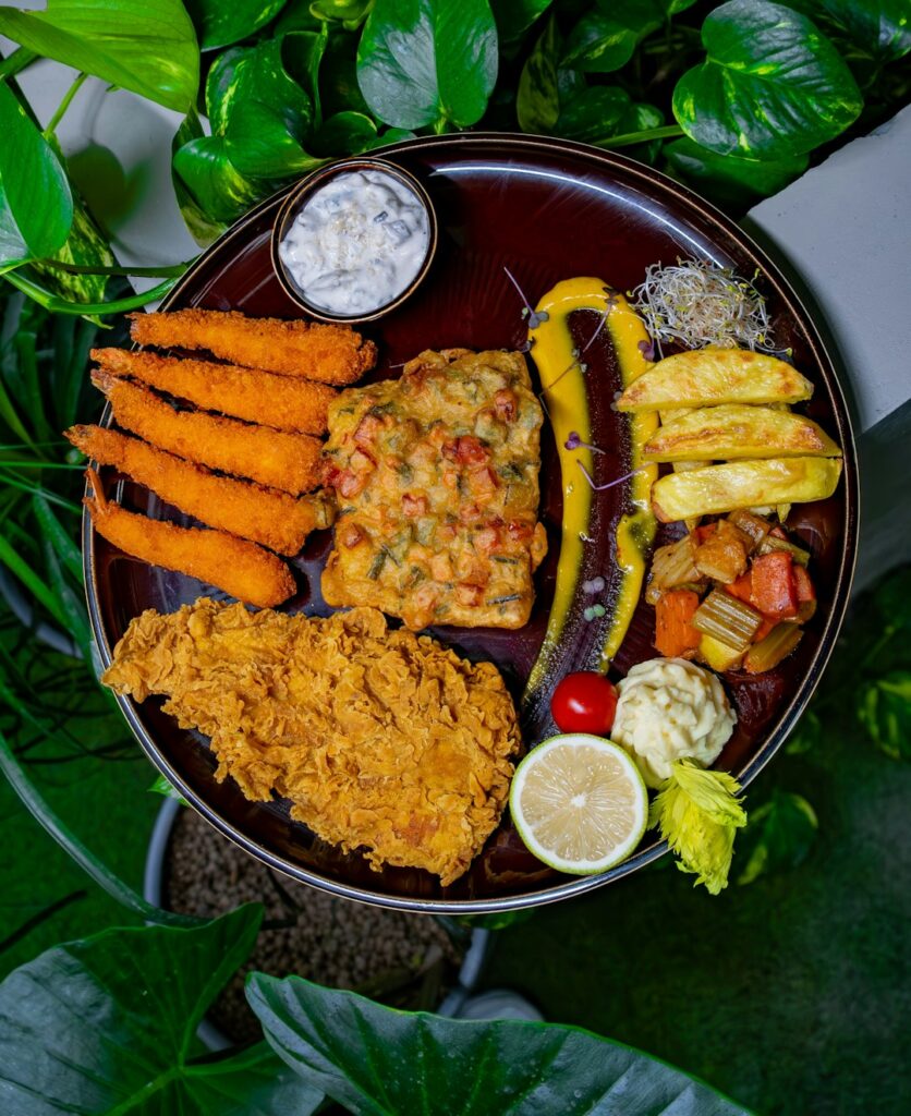 A mixed seafood platter with golden shrimp, fried fish, hush puppies, coleslaw, lemon wedges, and dipping sauce.